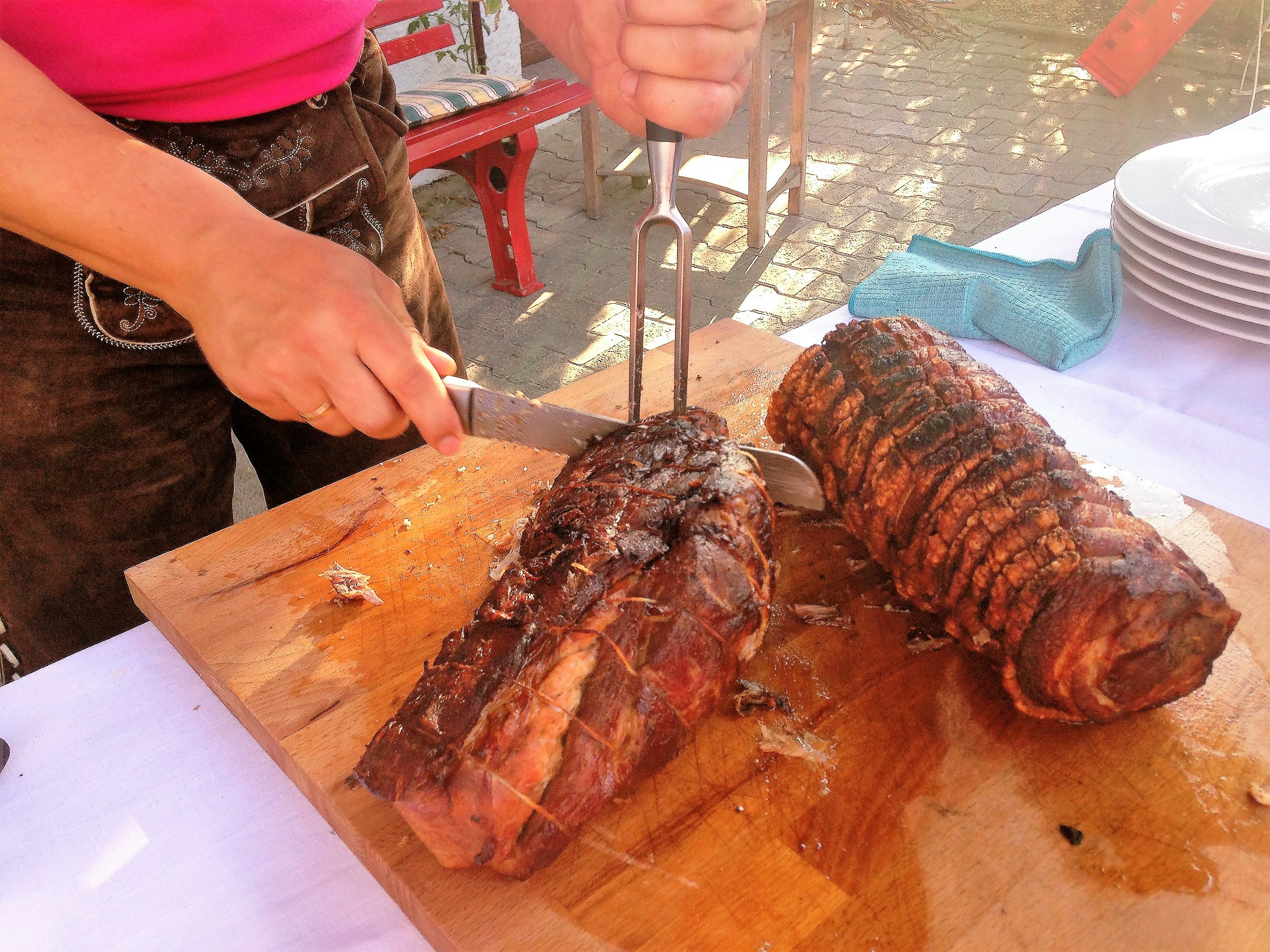 der-krosse-schweinebraten-wird-von-einem-Servicmitarbeiter-der-in-lhirschederhose-gekleidet-ist-aufgeschnitten-und-auf-teller-gelegt-dazu-gibt-es-natursoße