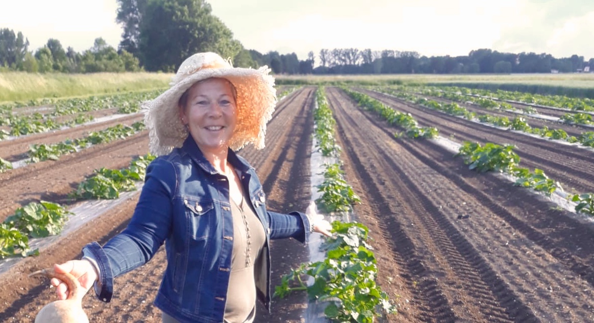 Gerlinde Schreyer steht am Kürbisfeld mit über 100 Sorten und hält eine Kalebasse (Flaschenkürbis) in der Hand. Die Kürbisse wachsen in Reihen auf verrottbarer Mulchfolie als nachhaltige Alternative zu Plastik