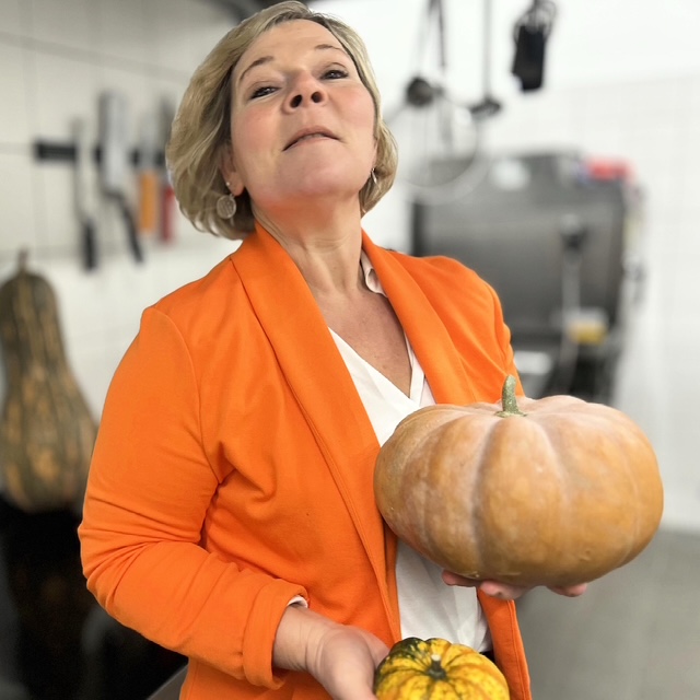 gerlinde-hält-eine-muscat-kuerbis-in- der-hand-in-schoenem-businessoutfit-orangen-blazer